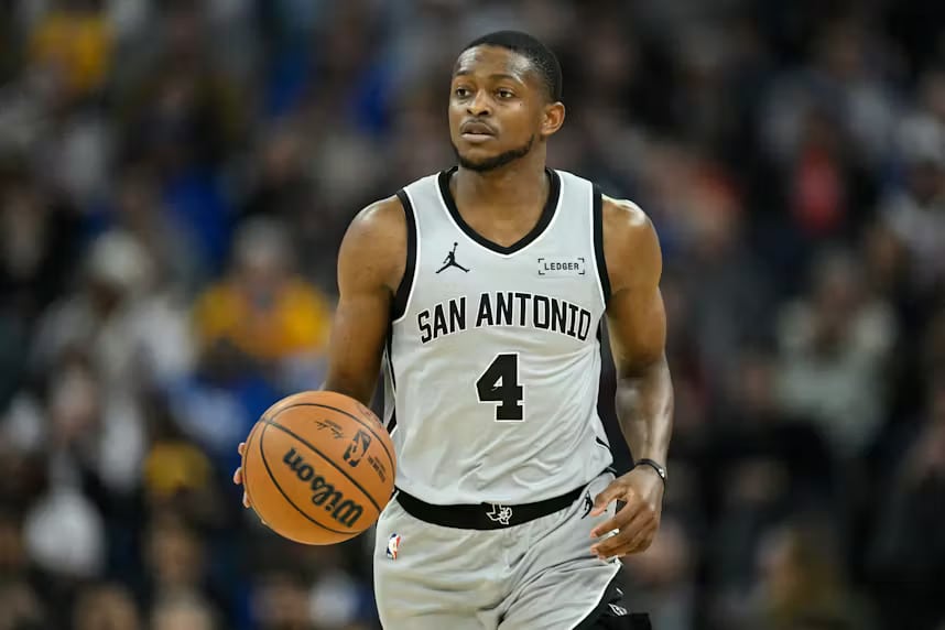 number 4 - Digital Wager Wire Basketball player in a white San Antonio jersey with the number 4 dribbling the ball during a game, with a blurred crowd in the background.