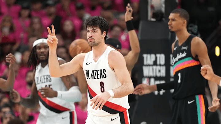spurs vs blazers - Digital Wager Wire Portland Trail Blazers player #8 raises two fingers in a peace sign during a game, with teammates and opponents in the background inside a crowded arena.