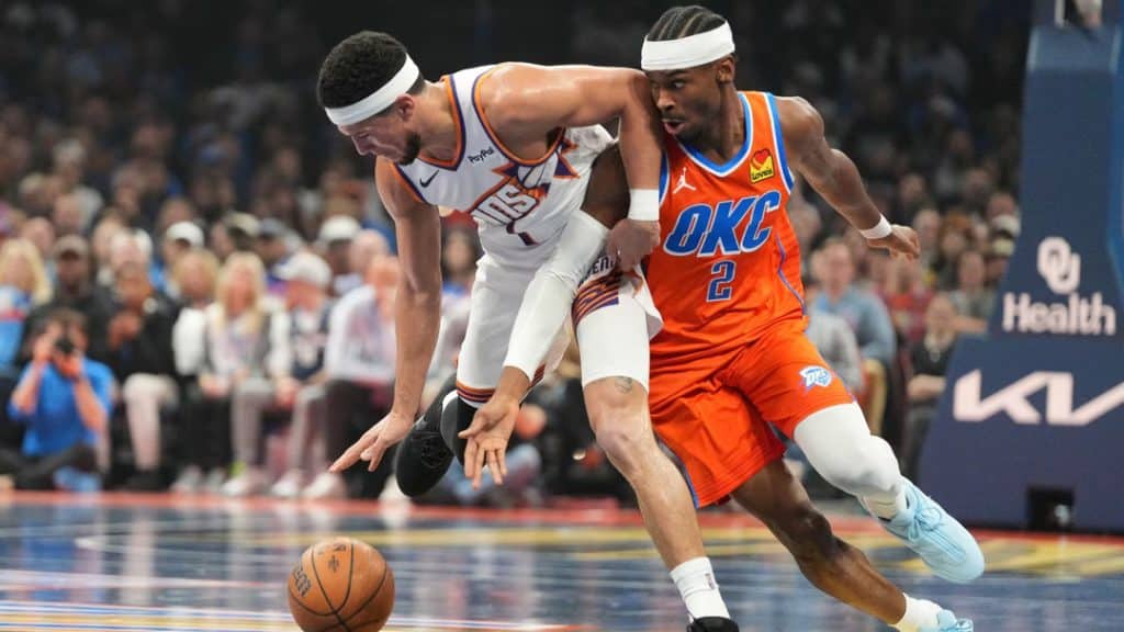 suns vs okc 1 - Digital Wager Wire Two basketball players reach for a loose ball during a fast-moving play on a crowded court, both leaning forward in pursuit.