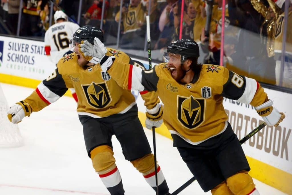 VEGAs - Digital Wager Wire Two Vegas Golden Knights players in gold jerseys celebrate on the ice, embracing and cheering after a likely goal, hockey sticks raised.