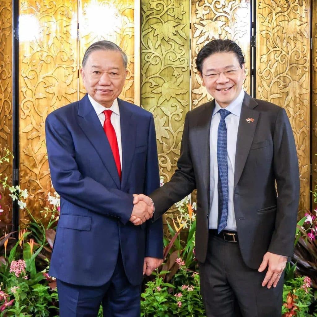 ceo japan banks shake hand - Digital Wager Wire Two men in business suits shake hands in front of an ornate wooden panel backdrop with flowers at the base, signaling a formal meeting or agreement.