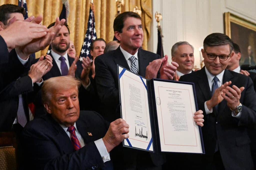 plans on stable coins 1 - Digital Wager Wire A man in a dark suit holds up a framed, signed document while others applaud in a formal room with gold curtains behind them.
