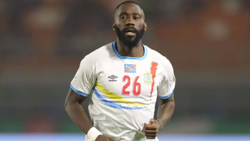 arthur of congo - Digital Wager Wire Bearded male footballer wearing a white jersey with blue trim and the number 26, running on a field during a match.