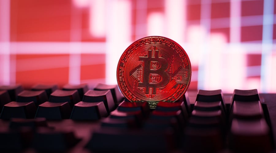 bitcoin is down - Digital Wager Wire Bitcoin coin resting on a computer keyboard with a red-tinted financial chart in the background, symbolizing cryptocurrency trading