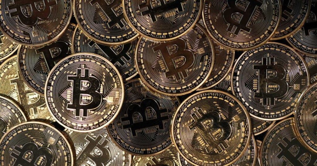 bitcoins on hand - Digital Wager Wire Close-up of numerous shiny gold Bitcoin coins piled together, showing the BTC symbol on each coin's face, conveying cryptocurrency wealth/collection.