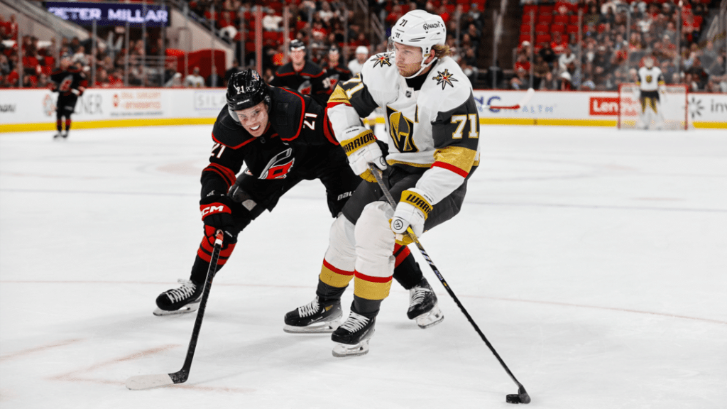 defending each other - Digital Wager Wire Two ice hockey players battle for the puck on the rink, one in a black uniform and the other in white and gold.
