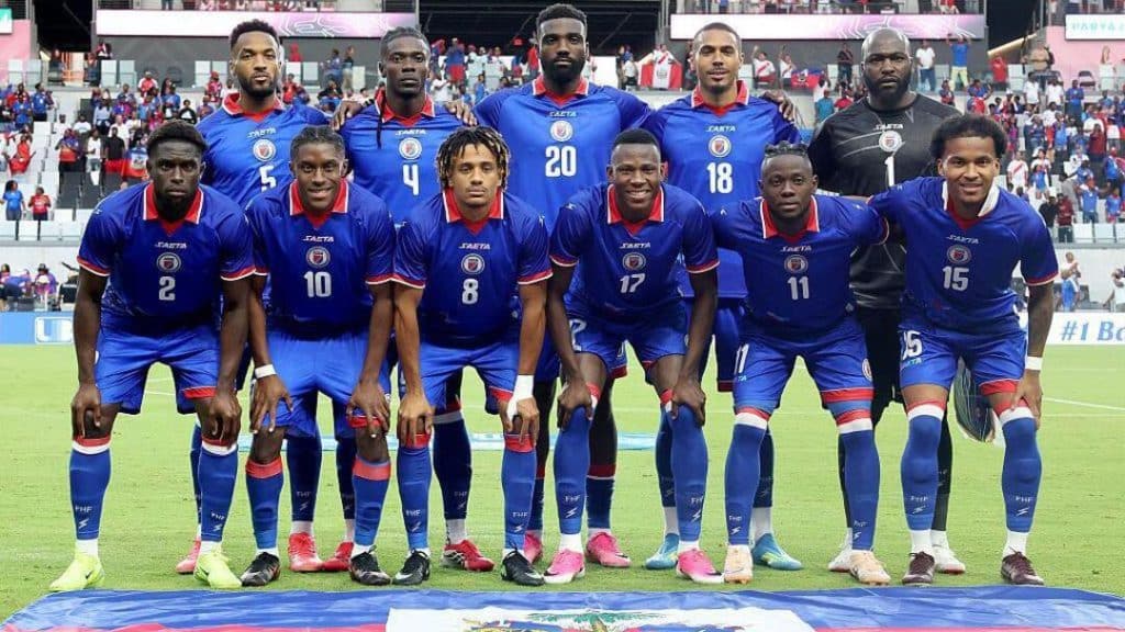 haiti world cup - Digital Wager Wire Soccer team in blue uniforms lined up for a pre-match photo on the field, players kneeling and standing with numbers visible on jerseys.