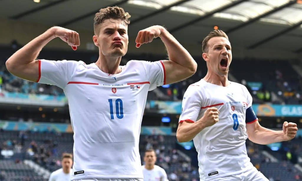 patrick - Digital Wager Wire Two male soccer players in white uniforms celebrate on the field, flexing their arms and shouting.",