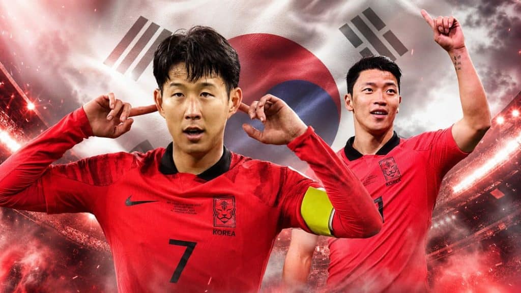 south korea - Digital Wager Wire Two male footballers in red South Korea jerseys celebrate, one wearing a captain's armband, with a Korea flag backdrop.