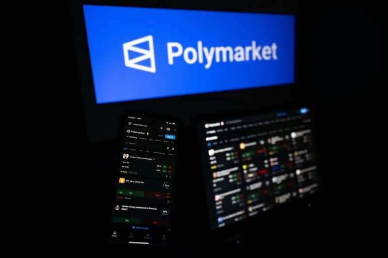 polymarket website - Digital Wager Wire Polymarket logo on a blue screen above two monitors displaying trading dashboards in a dark room.