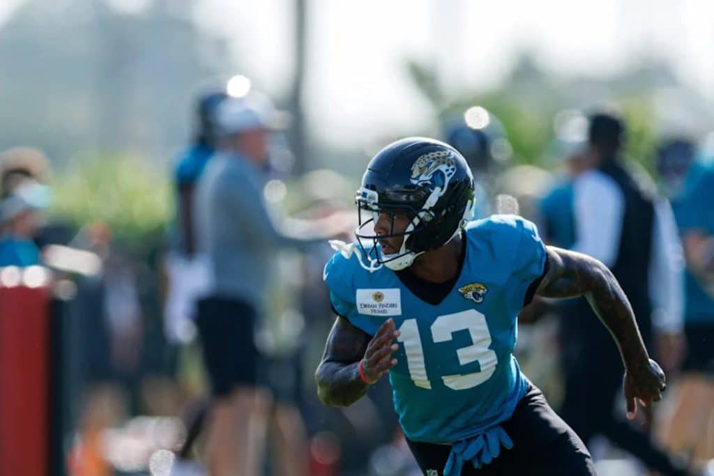 JAGUAR PLAYER RUNs - Digital Wager Wire Football player in teal practice jersey and helmet sprinting on the field during training drill, #13 visible on jersey.