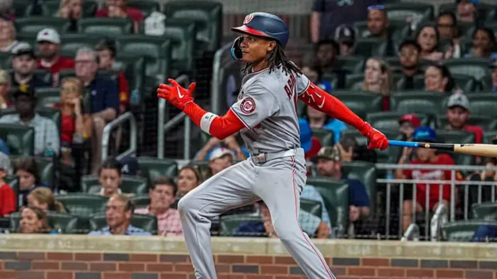 nationals mlb - Digital Wager Wire Baseball player in gray and red uniform mid-swing at the plate as spectators watch from the stands.