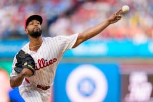 phillies - Digital Wager Wire Phillies pitcher in a white pinstripe uniform throwing a fastball mid‑stride toward home plate.