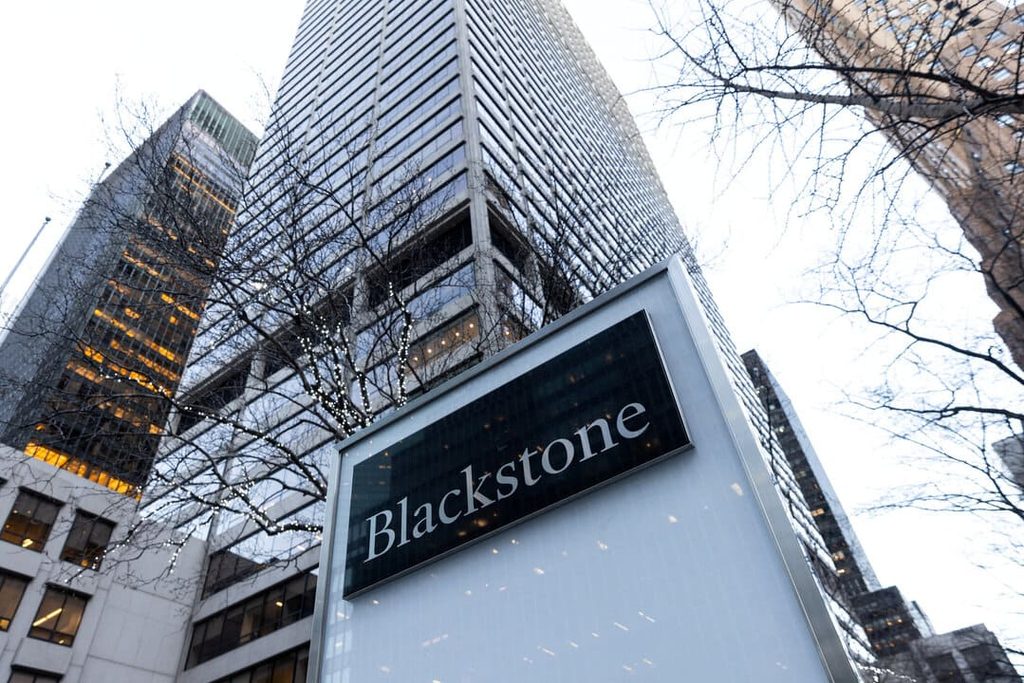 shadow banks - Digital Wager Wire Low-angle shot of a Blackstone sign with tall glass skyscrapers and bare trees in winter, city scene behind.