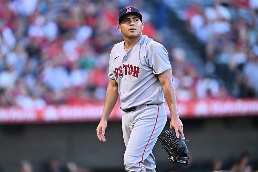 Baseball pitcher for the Boston Red Sox walking on the mound with a glove in hand as fans watch.