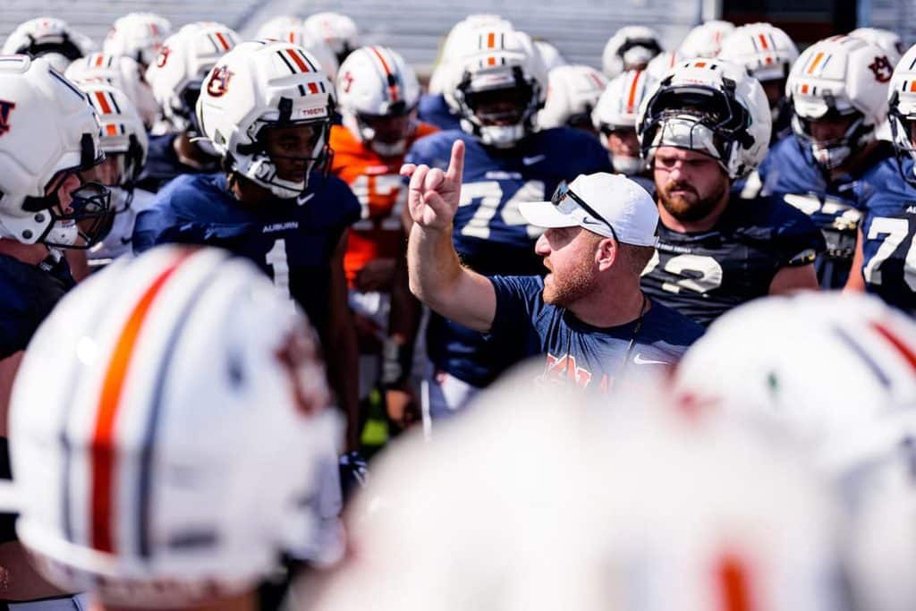 Coach in a navy shirt giving directions to a football team gathered in a huddle during practice.