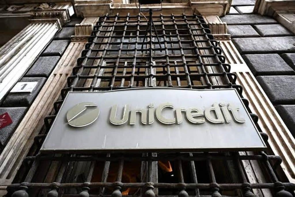 unicredit - Digital Wager Wire Unicredit bank sign behind a metal security grille on a stone building surface.