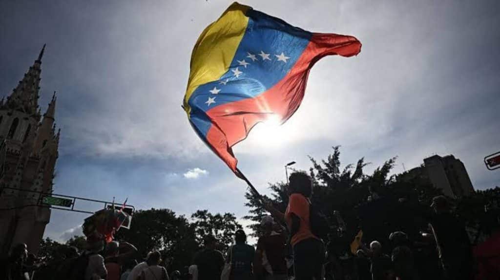 venezuelan flag - Digital Wager Wire Venezuelan flag waved above a crowd during a street protest, sun behind the flag creating a silhouette.