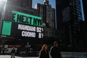 comercial ads war - Digital Wager Wire Green billboard with large black-and-white text 'MAMDANI 92% CUOMO 8%', against an urban skyline; pedestrians in foreground.